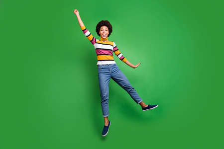 Full body photo of funky cheerful girl jump hold hand umbrella blowing windy weather scream enjoy wear bright denim jeans isolated over green color backgroundの写真素材