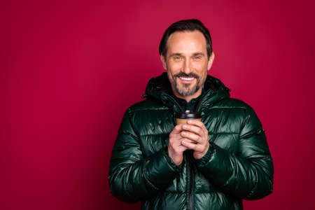 Photo of stylish trendy man smiling toothily holding cup of coffee disposable standing near empty...