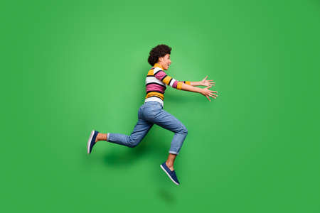 Come here dear friend. Full length profile side photo of crazy afro american girl see her best buddy jump run want hug hands wear denim jeans shine outfit isolated green color backgroundの写真素材