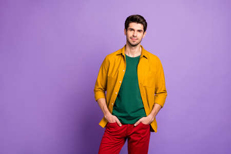 Photo of confident serious man standing with hands in pockets of red pants looking at you isolated violet pastel color backgroundの写真素材