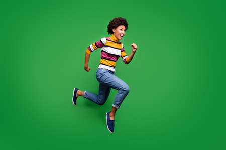 Full body profile side photo of crazy cheerful afro american girl jump run after fall discounts feel rejoice emotions wear bright clothing blue sneakers isolated over green color backgroundの写真素材