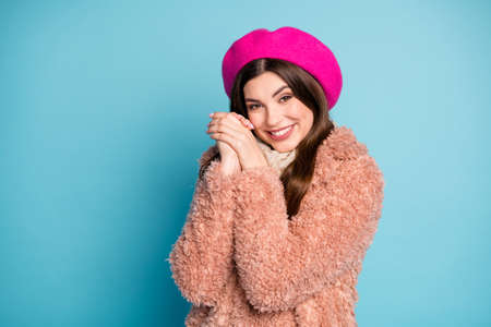 Portrait of glad dreamy girl in bright beret enjoy winter cold weather feel grateful hold fists near face wear fur pastel overcoat isolated over blue color backgroundの写真素材