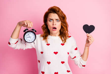 Close-up portrait of her she nice attractive pretty cute lovely worried nervous wavy-haired girl holding in hand black heart bell clock trouble stress isolated on pink pastel color backgroundの写真素材