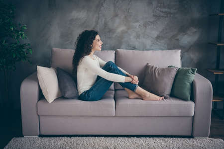 Profile side view of her she nice-looking attractive sweet lovely cheerful cheery wavy-haired girl sitting on divan spending day in modern loft industrial style interior living-room indoorsの写真素材