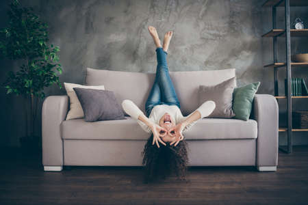 Portrait of her she nice attractive crazy glad cheerful cheery wavy-haired girl having fun lying, divan showing ok-sign like glasses in modern loft industrial style interiorの写真素材