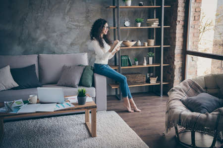 Full length body size view of her she nice attractive lovely cheerful cheery wavy-haired girl writing good ideas in note pad in modern loft industrial style interior living-room indoorsの写真素材