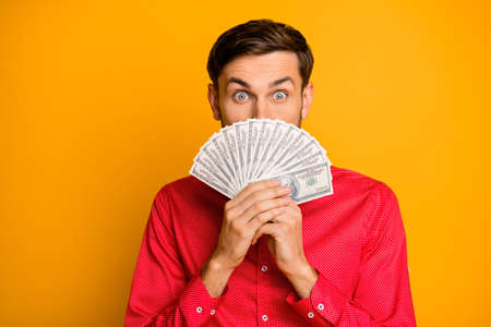 Photo of attractive funny guy hold fan of usa bucks hide mouth crazy smile rich person wear trendy red shirt bow tie clothes isolated yellow color backgroundの写真素材