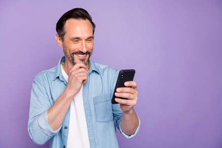Portrait of cheerful man use cellphone get message from his wife read post enjoy wear casual style clothes isolated over violet color backgroundの写真素材