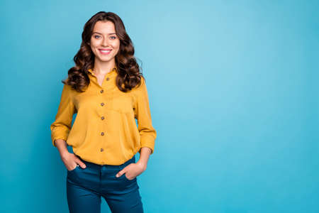 Photo of amazing curly business lady hold hands in pockets toothy beaming smiling best chief worker wear yellow shirt trousers isolated blue color backgroundの写真素材