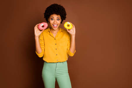 Photo of funny pretty dark skin curly lady hold two colorful donuts with caramel eyes human faces...
