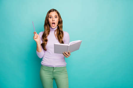 Photo of beautiful crazy excited wavy lady hold planner have creative business idea hold pencil open mouth wear lilac sweater green pants isolated teal pastel color backgroundの写真素材