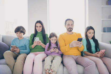 Portrait of nice attractive lovely charming big full focused family pre-teen kids sitting on divan using 5g app blogging post smm media browsing web service at light white interior style houseの写真素材