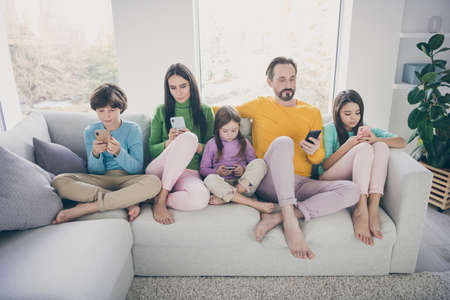Portrait of nice attractive bare foot big full focused family pre-teen kids sitting on divan using...