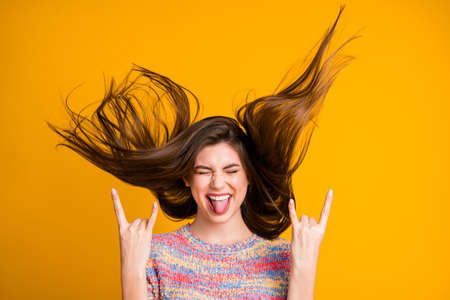 Portrait of crazy funky excited girl rock fan make horned symbol show tongue out close eyes enjoy rejoice her hairdo flying wear pullover isolated over bright shine yellow color backgroundの写真素材