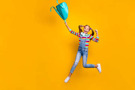 Yeah i pass exams. Ful size photo crazy energetic ecstatic schoolkid jump throw blue bag rucksack wear striped sweater denim casual style jeans isolated bright shine yellow color backgroundの写真素材