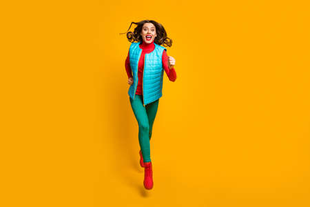Full length photo of excited girl jump run move fast after autumn winter sales wear green blue red...