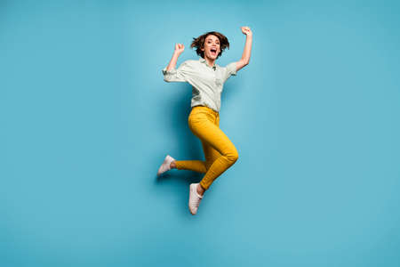 Full size photo of funky lady jumping high up celebrating weekend vacation start beginning wear casual green shirt yellow pants shoes isolated blue color backgroundの写真素材