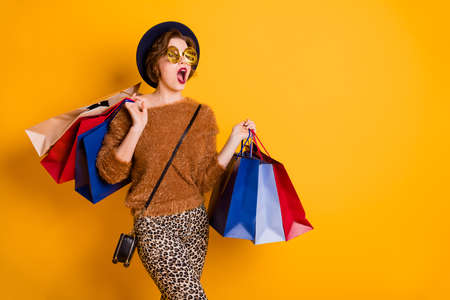 Photo of staring lady open mouth look empty space sales shopping center many packs wear soft sweater leopard pants retro cap shoulder bag specs isolated yellow color backgroundの写真素材
