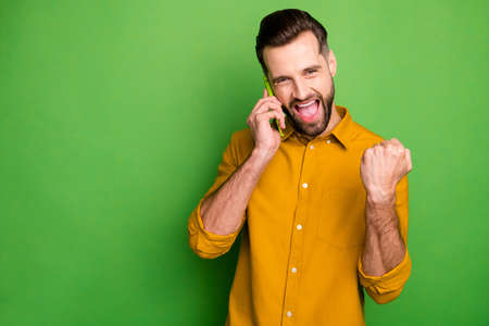 Close-up portrait of nice attractive cheerful cheery glad satisfied guy in formal shirt discussing great news on cell isolated on bright vivid shine vibrant green color backgroundの写真素材
