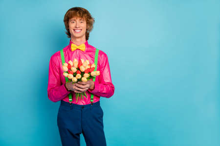 Portrait of positive cheerful guy hold bunch with fresh natural tulips he prepare for his girlfriend celebrate 8-mrach event wear good look pants outfit isolated over blue color backgroundの写真素材