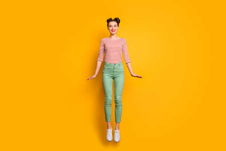 Full length photo of attractive pretty lady jumping high up rejoicing traveler abroad wear red white pullover shirt green pants footwear isolated bright yellow backgroundの写真素材
