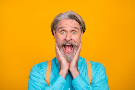 Closeup photo of funny stylish clothes crazy grandpa open mouth see sale shopping advert arms on cheekbones wear blue shirt suspenders bow tie, isolated yellow color backgroundの写真素材