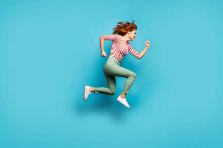 Full body profile photo of funny lady jump high speed rushing black friday season shopping wear casual red white shirt green trousers footwear isolated blue color backgroundの写真素材