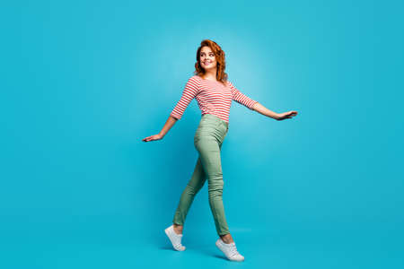 Full length profile photo of funny pretty lady enjoy warm spring day spend time walk street wear casual red white shirt green pants shoes isolated blue color backgroundの写真素材