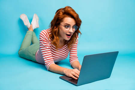 Full size close up photo crazy woman lie floor work laptop get incredible blogging notification impressed scream wow omg wear good look sneakers isolated blue color backgroundの写真素材