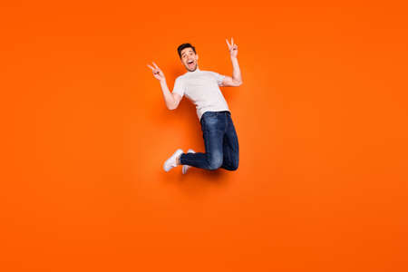 Full size photo of positive cheerful guy jump enjoy spring free time holidays make v-sign wear casual style stylish outfit gumshoes isolated over bright color backgroundの写真素材