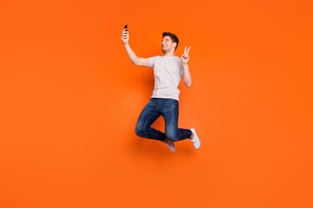 Full length profile photo of funky guy jump high up rejoicing make selfies show v-sign symbol wear...