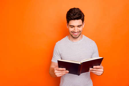 Photo of funny attractive guy hold favorite book hands enjoy reading exciting final intrigue wear striped t-shirt isolated bright orange color backgroundの写真素材