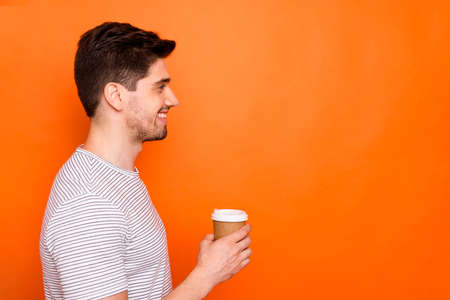 Just for you. Profile photo of funny attractive macho guy hold hand hot takeout coffee beverage look side empty space wear striped t-shirt isolated vivid orange color backgroundの写真素材