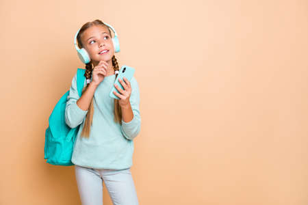 Photo of beautiful little lady listen earphones favorite song walk school hold telephone think dream about weekend wear blue pullover jeans isolated beige color backgroundの写真素材