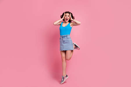 Full length photo of pretty funny crazy lady jump high up arms on head look sale black friday advert wear blue tank-top denim short skirt shiny footwear isolated pink color backgroundの写真素材
