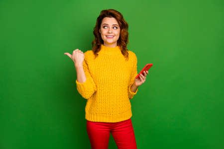 Portrait of positive cheerful woman social network promoter point thumb finger direct way adverts promotion use smartphone wear sweater pants isolated over bright shine color backgroundの写真素材