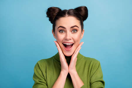 Closeup photo of attractive crazy lady two funny buns good mood open mouth arms on cheeks wear warm green turtleneck pullover isolated blue color backgroundの写真素材