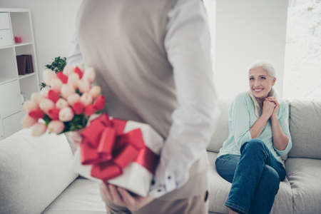 Mans hands hold tulips bunch and giftbox behind back making romantic surprise for waiting with...