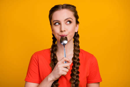 Photo of pretty teenager lady hold metal spoon in mouth desire dinner look dreamy empty space think of tasty food wear casual red t-shirt isolated vivid yellow color backgroundの写真素材