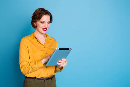 Photo of pretty business lady hold tablet hands freelancer worker reading corporate report company website wear yellow shirt green pants isolated bright blue color backgroundの写真素材