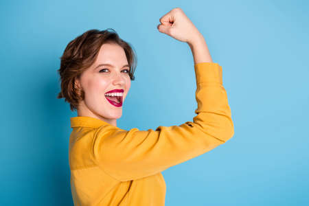 Profile photo of pretty cheerful lady hold raise biceps hand arm show perfect biceps gym training strong powerful woman wear yellow shirt isolated bright blue color backgroundの写真素材