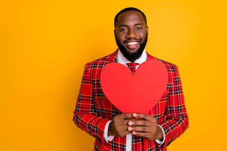 Photo of cute dark skin guy hold hands paper heart figure asking inviting girlfriend romance date wear plaid red costume blazer shirt tie isolated yellow color backgroundの写真素材