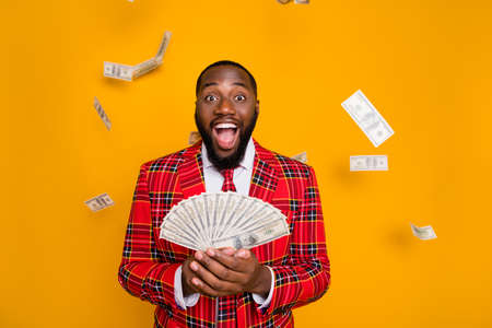 Photo of excited dark skin guy hold hands fan of usa bucks rich person millionaire money falling wear plaid red costume blazer shirt tie isolated yellow color backgroundの写真素材