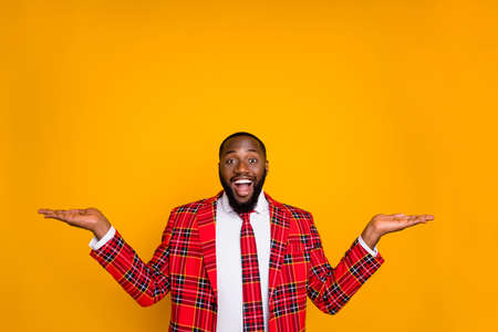 Photo of funny dark skin guy hold two open palms empty space advising novelty products discount offer price wear plaid costume blazer shirt tie isolated yellow color backgroundの写真素材