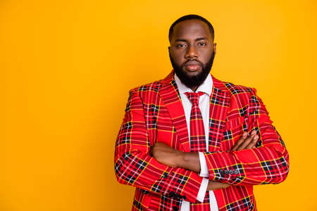 Photo of attractive dark skin guy look seriously arms crossed not smiling strict boss person wear plaid red costume blazer white shirt isolated bright yellow color backgroundの写真素材