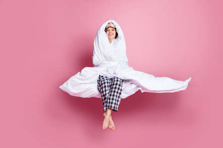 Full body photo of cheerful lady satisfied enjoy morning sitting bed hug warm blanket eyes closed wear mask white plaid pajama pants barefoot isolated pink color backgroundの写真素材