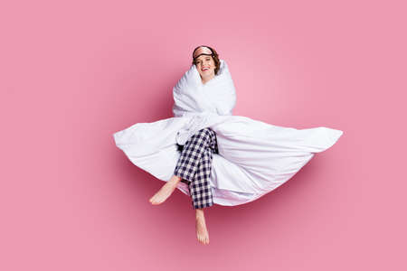 Full length photo of cheerful funny lady satisfied morning sitting bed hug warm blanket wear mask...
