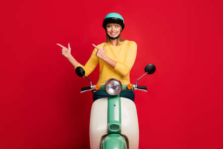 Portrait of her nice attractive lovely girlish cheerful cheery glad girl sitting on moped showing copy space solution isolated on bright vivid shine vibrant red color backgroundの写真素材