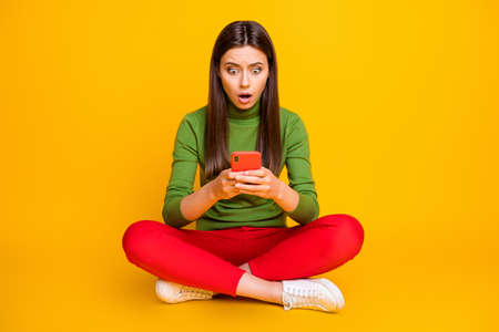 Oh no. Photo of beautiful lady sit floor holding telephone hands not believe eyes internet blog blocked wear green sweater red trousers isolated yellow color backgroundの写真素材