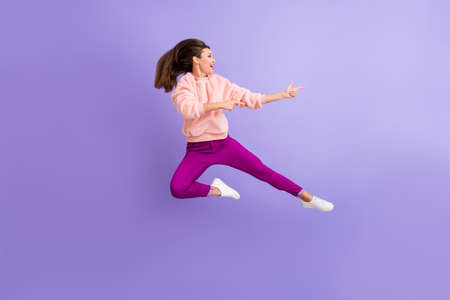 Full length profile photo of cheerful lady jumping high indicating fingers empty space amazing sale wear casual fluffy pullover pants shoes isolated purple color backgroundの写真素材